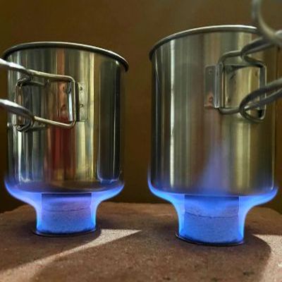 Two steel mugs heating side by side on the PillBottle Stones Stove, blue flames under each